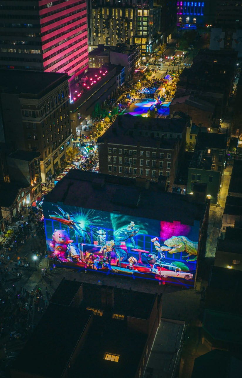 The illuminated Kenner toy mural at BLINK Cincinnati within the city at night.